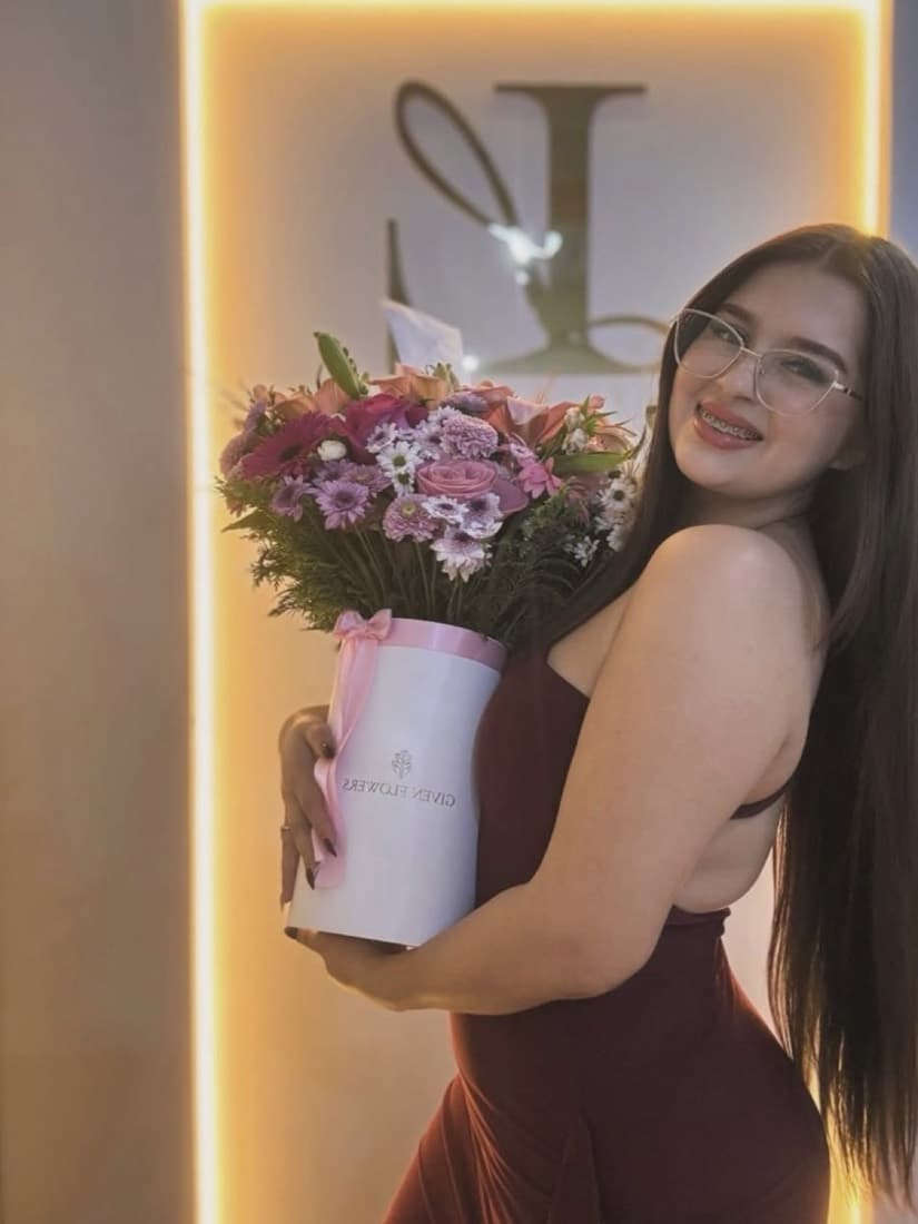 Liz con un ramo de flores frente al cartel iluminado de Liz Boutique