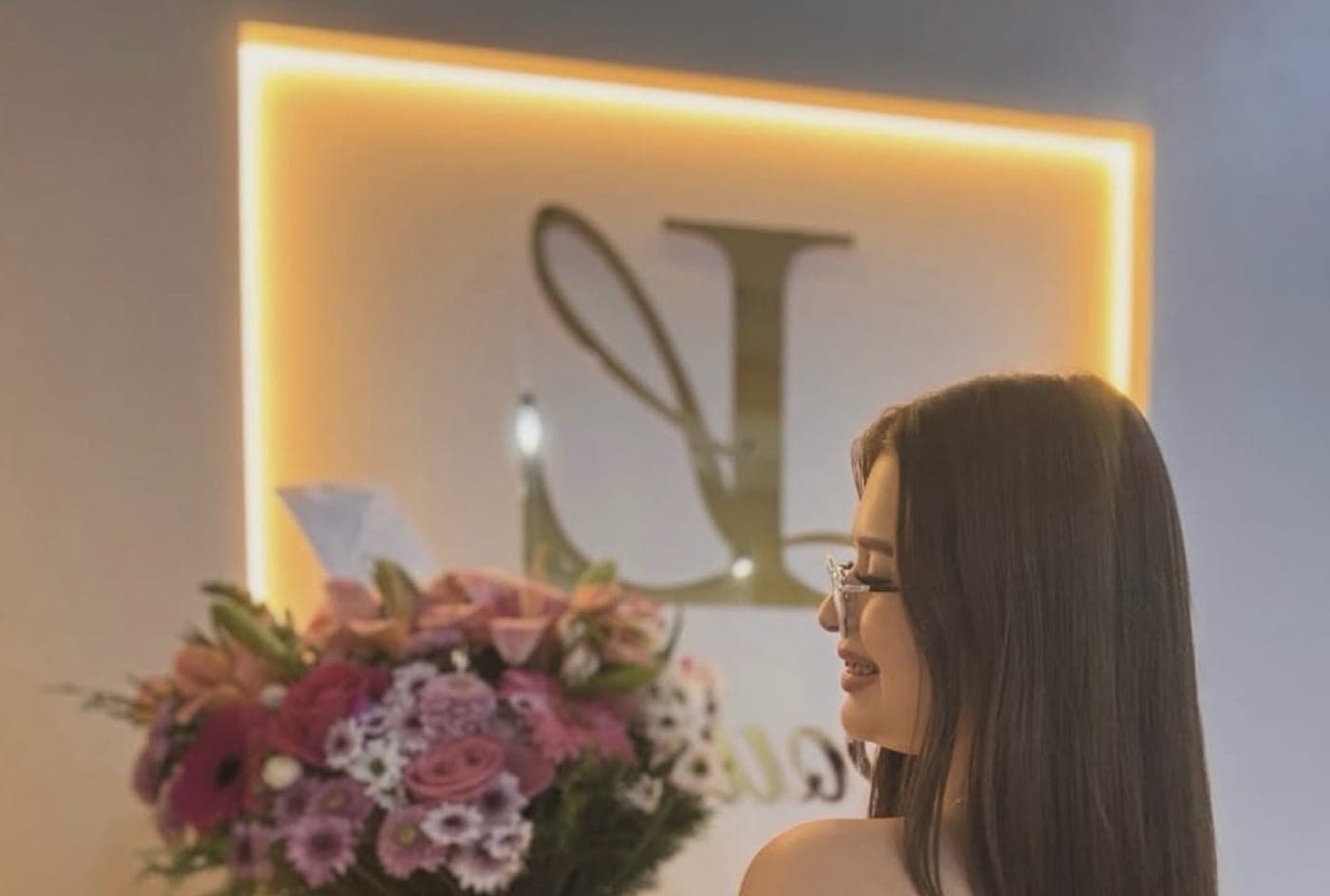 Liz at the Liz Boutique store, next to the illuminated sign with the golden L